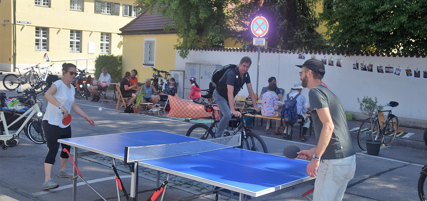 Buntes Treiben Tischtennispartie und Menschen im Hintergrund, die am Straßenrand sitzen.