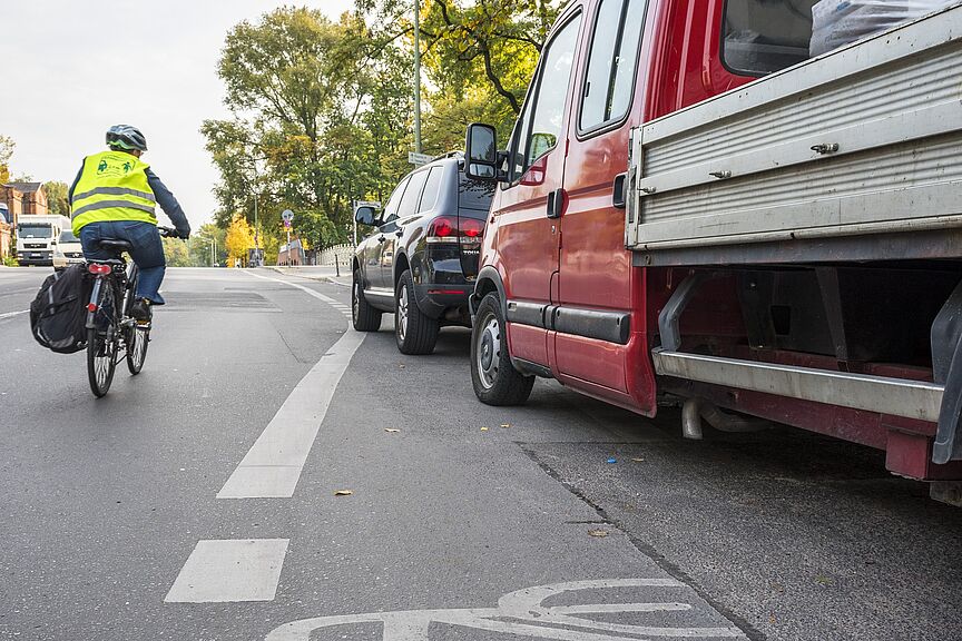Blockierter Radweg Ein Radschutzstreifen wird von Pkws blockiert, während eine Radfahrerin in die Mitte ausweichen muss.