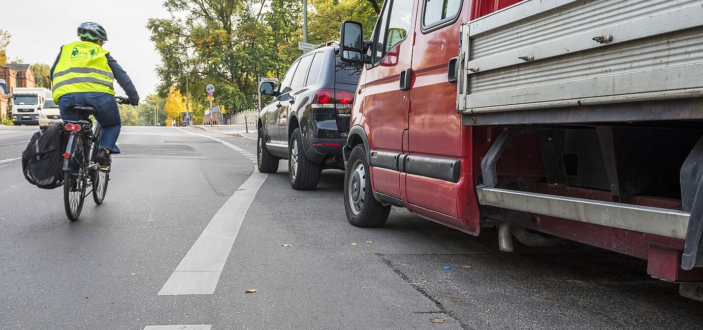 Ein Radschutzstreifen wird von Pkws blockiert, während eine Radfahrerin in die Mitte ausweichen muss.