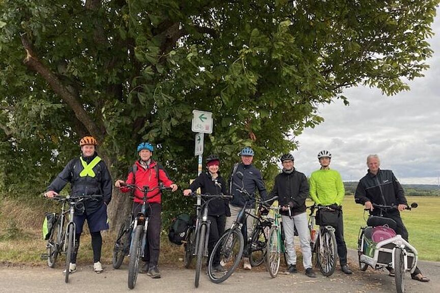 Gruppenfoto der ADFC Ausfahrt 2024 Sieben Radfahrende posieren mit ihren Fahrrädern vor einer grossen Eiche am Lahnradweg kurz vor Fronhausen.